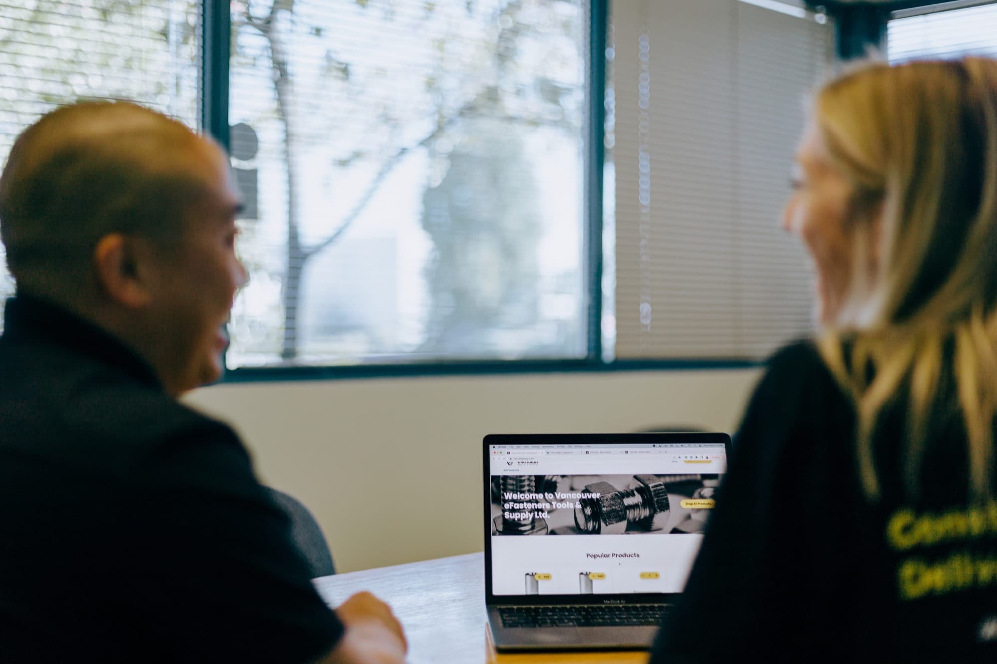Two people at an office table reviewing a dealer's storefront on a laptop