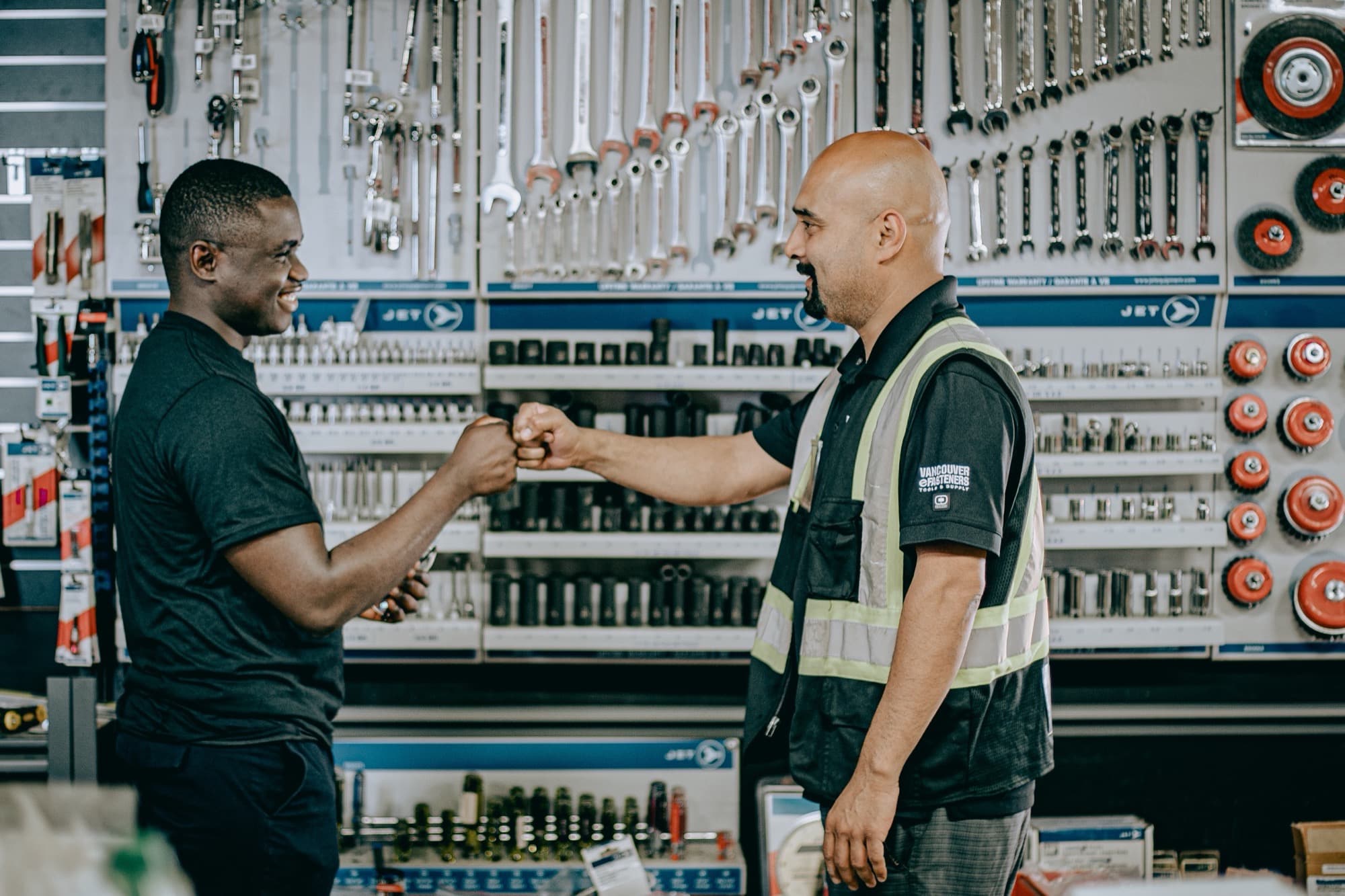 A dealer's staff member and a contractor bumping fists across the counter of a tool supply store.