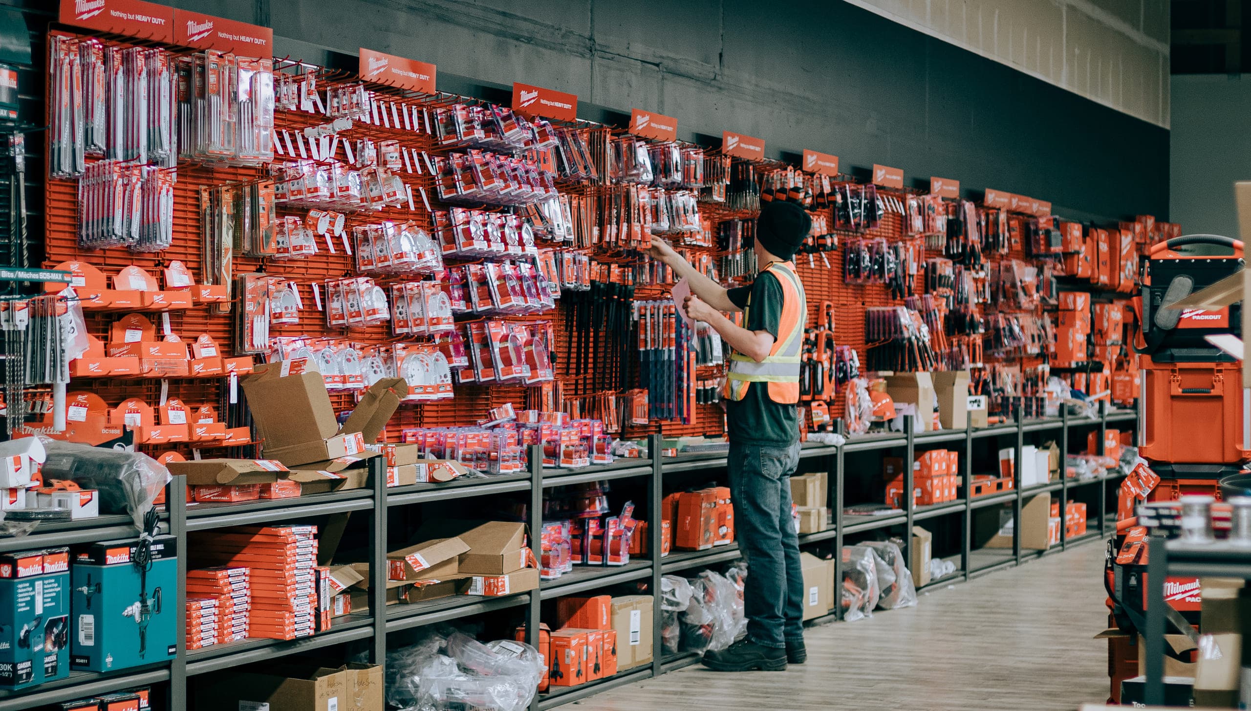 A dealer's team member in a safety vest restocking a packed tool wall in the store aisle
