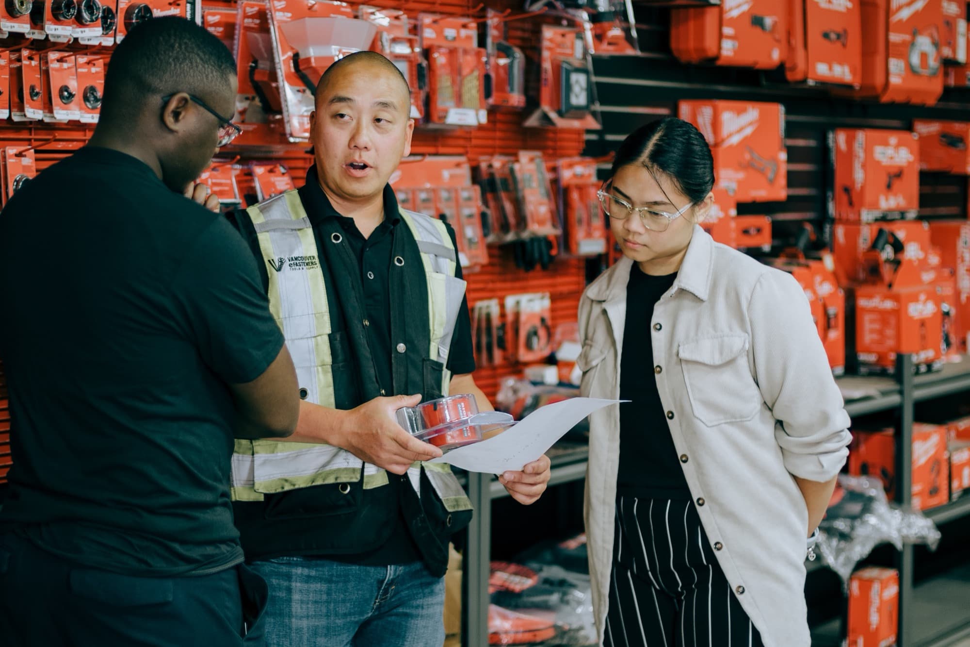 A hardware store staff member in a hi-vis vest going through an order with two customers