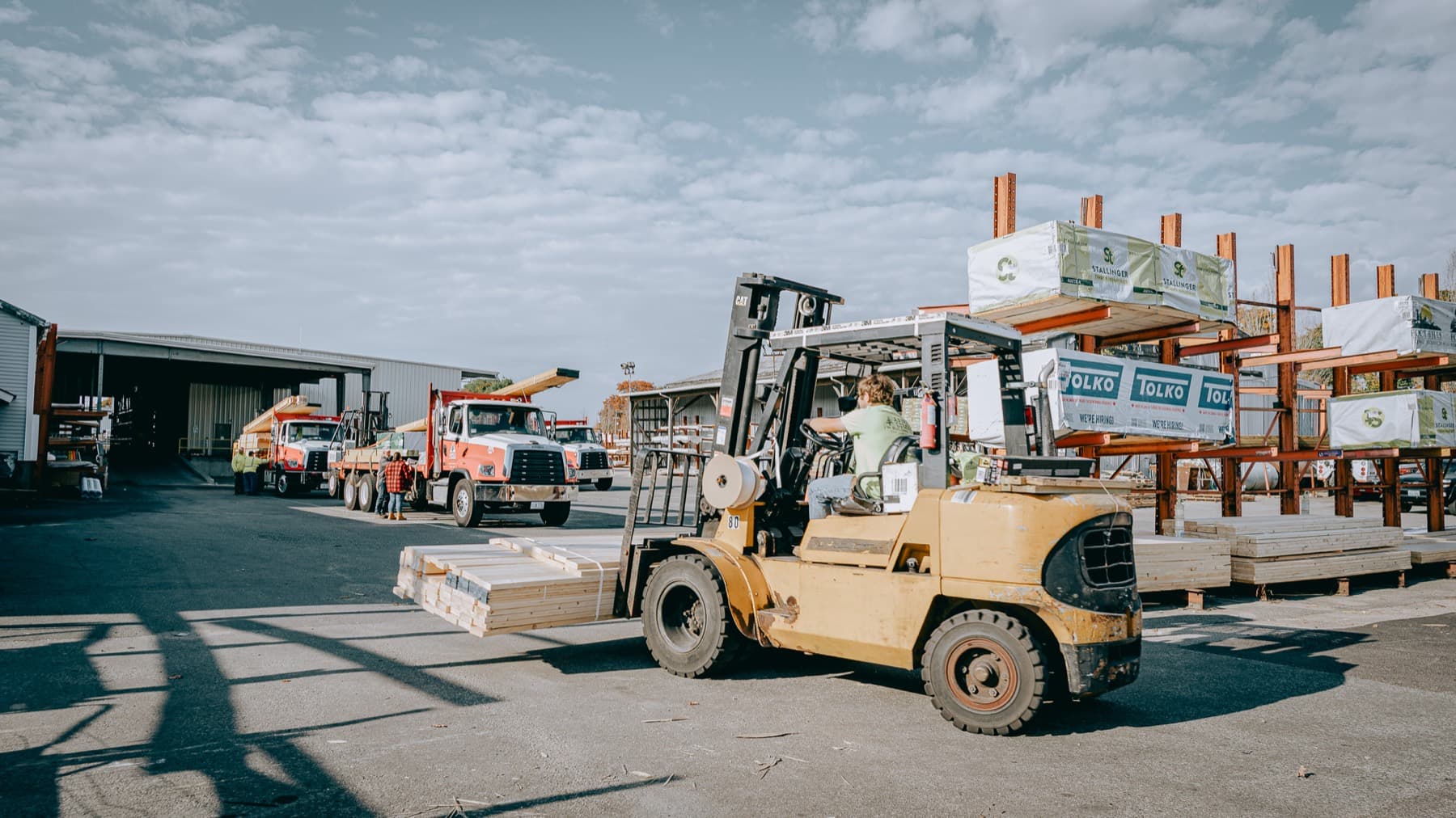 A forklift loading lumber at a dealer's yard, with flatbed trucks waiting
