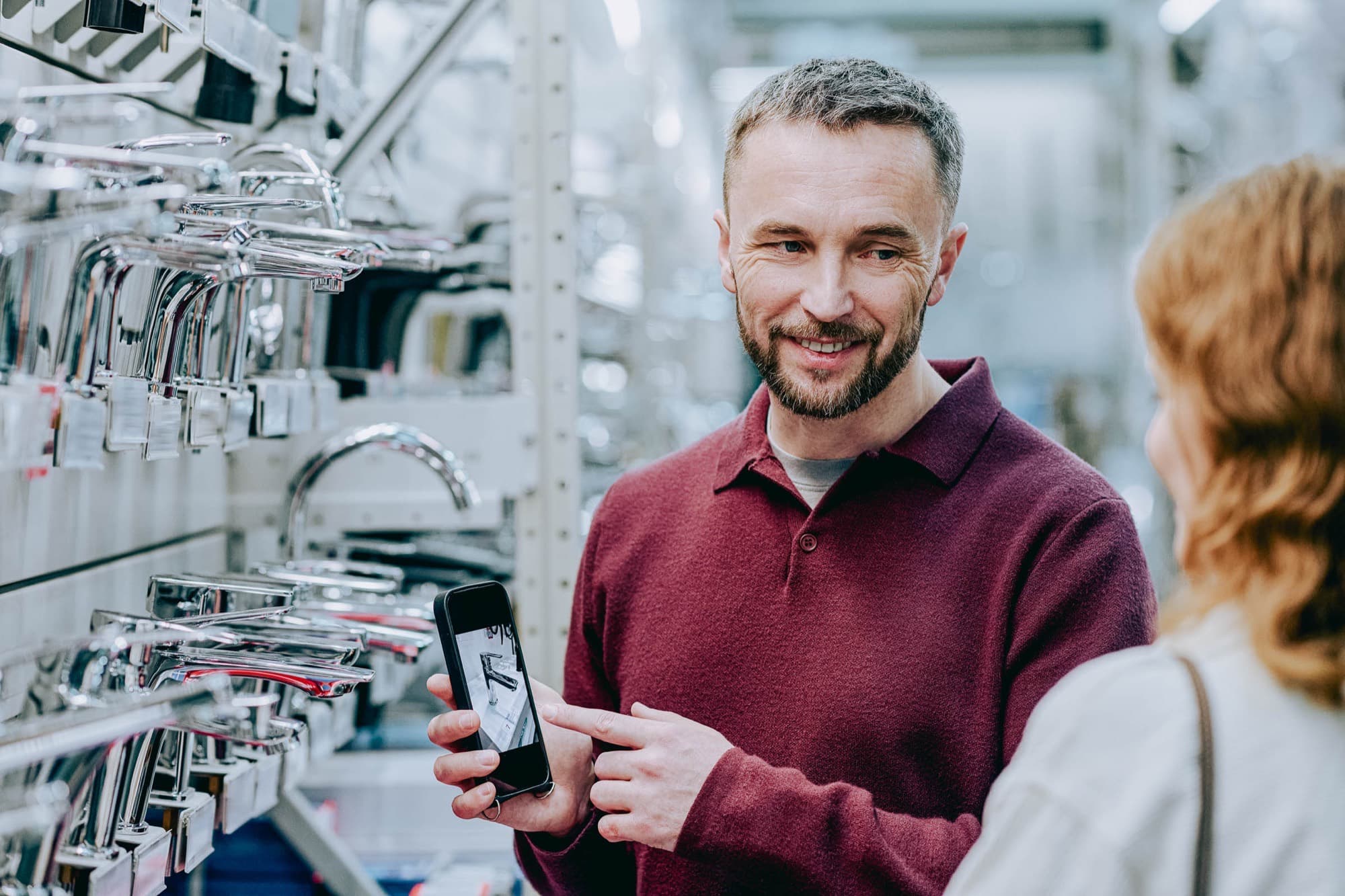 A supply house staff member showing a fixture on his phone to a customer in the faucet aisle